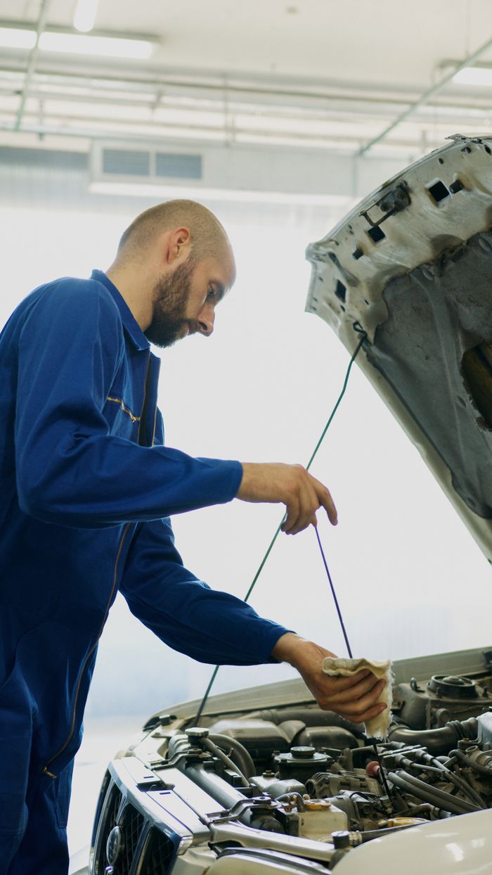 hero-img Mechanic inspecting car engine oil with dipstick in an automotive repair shop.